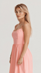 Femme blonde en robe rose élégante, posant de profil sur fond blanc. Mode féminine, style chic, tenue estivale.