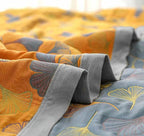 Couverture en coton réversible avec motifs de feuilles de ginkgo, tons orange et gris, design moderne, literie confortable et élégante.