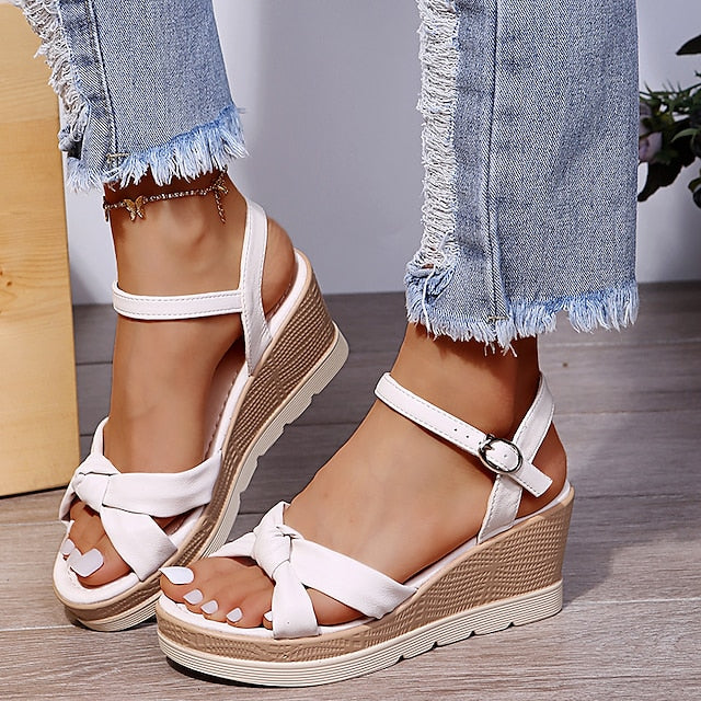 Sandales compensées blanches élégantes avec lanières croisées, portées avec un jean effiloché. Mode estivale, chaussures tendance pour femmes.