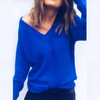 Femme portant un pull bleu vif à col en V, manches longues, posant avec une main dans les cheveux, style décontracté, mode automne-hiver.