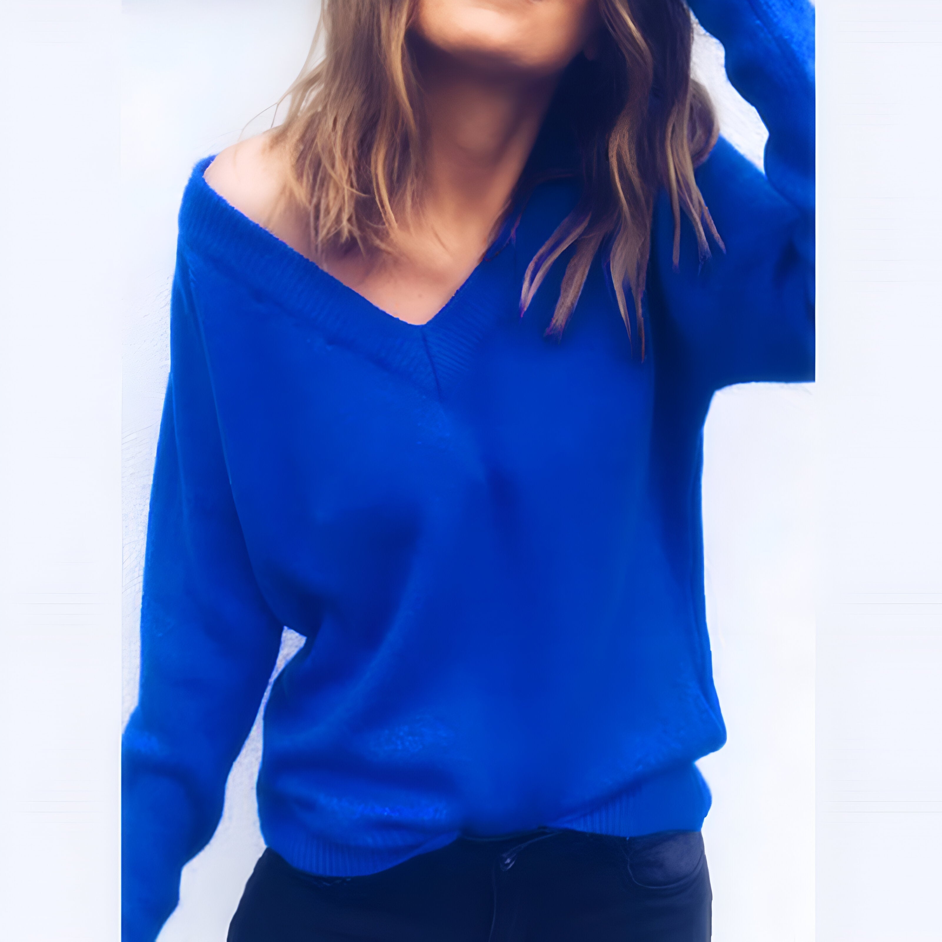 Femme portant un pull bleu vif à col en V, manches longues, posant avec une main dans les cheveux, style décontracté, mode automne-hiver.