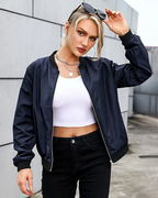 Femme en blouson bomber bleu marine, t-shirt blanc et jeans noir, posant avec lunettes de soleil. Mode urbaine, style décontracté, tendance féminine.