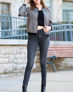 Femme portant un blouson gris, un top noir et un jean slim gris, posant devant un banc en pierre. Mode urbaine, style décontracté, tendance automne.