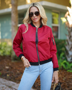 Femme blonde portant un blouson rouge et des lunettes de soleil, posant à l'extérieur. Mode décontractée, style urbain, tendance automne.