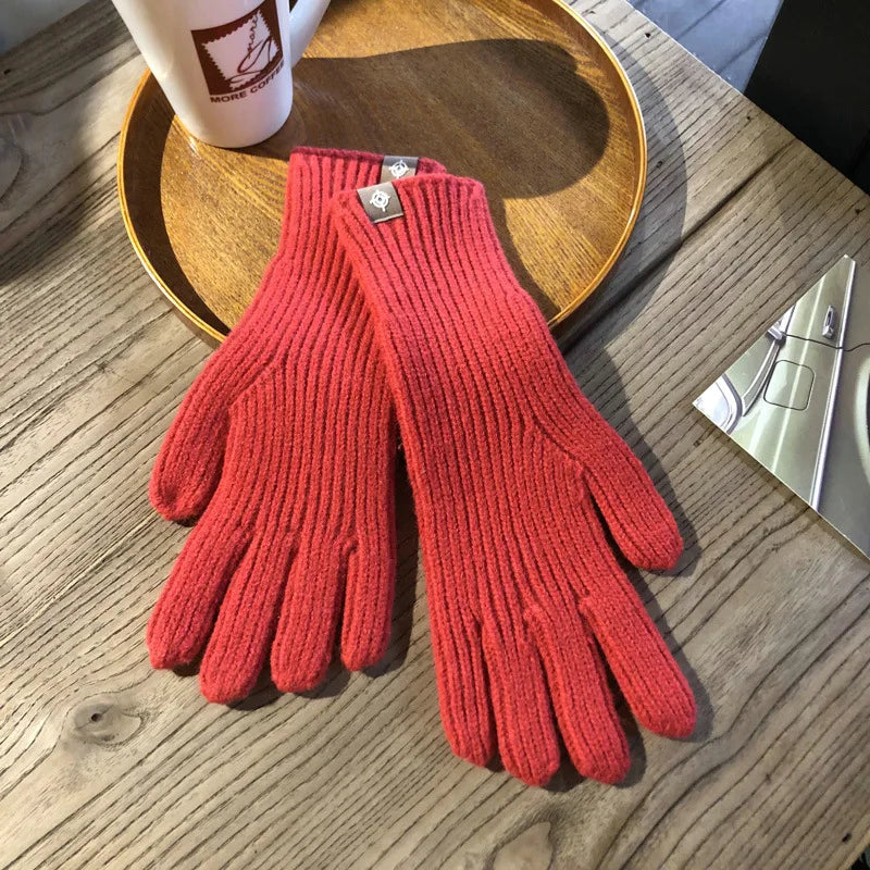 Gants rouges en laine posés sur une table en bois, à côté d'une tasse de café et d'un magazine. Accessoire d'hiver élégant et chaud.
