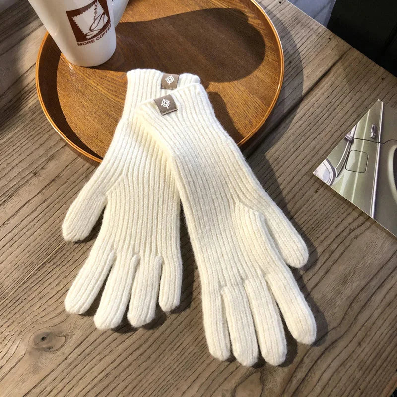 Gants en laine blanche sur une table en bois, posés sur un plateau rond en bois, à côté d'une tasse à café blanche. Accessoire hiver élégant.