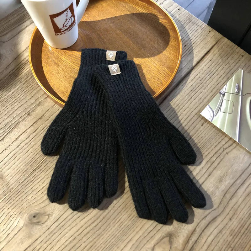 Gants en laine noirs élégants posés sur une table en bois, accompagnés d'une tasse de café et d'un plateau en bois. Accessoire hiver chic et chaud.
