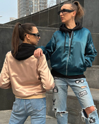 Deux femmes en vestes bomber satinées, l'une rose et l'autre bleue, posent sur des marches urbaines. Mode urbaine, lunettes de soleil, jeans déchirés.