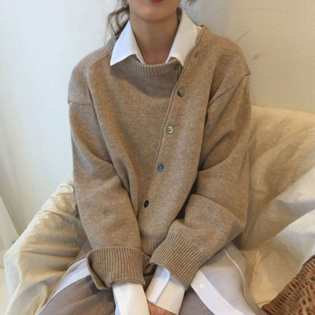 Femme portant un pull beige en laine avec chemise blanche, style décontracté chic, mode automne-hiver, assise sur un canapé beige.