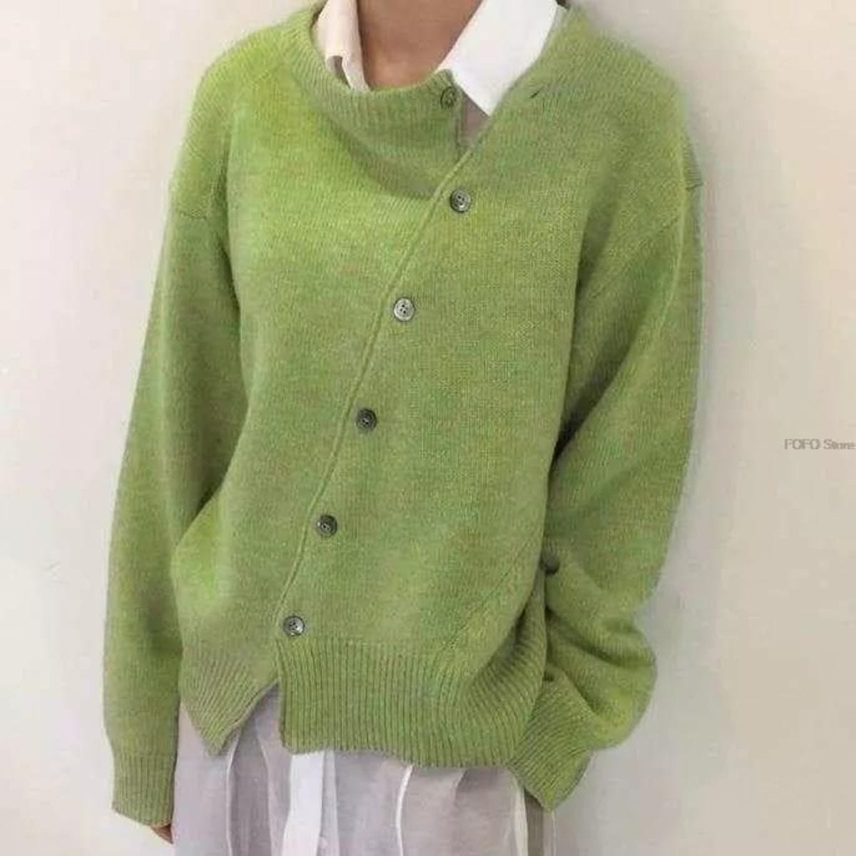 Cardigan vert asymétrique en laine, boutons décalés, porté sur une chemise blanche. Mode automne, style décontracté, tendance féminine.