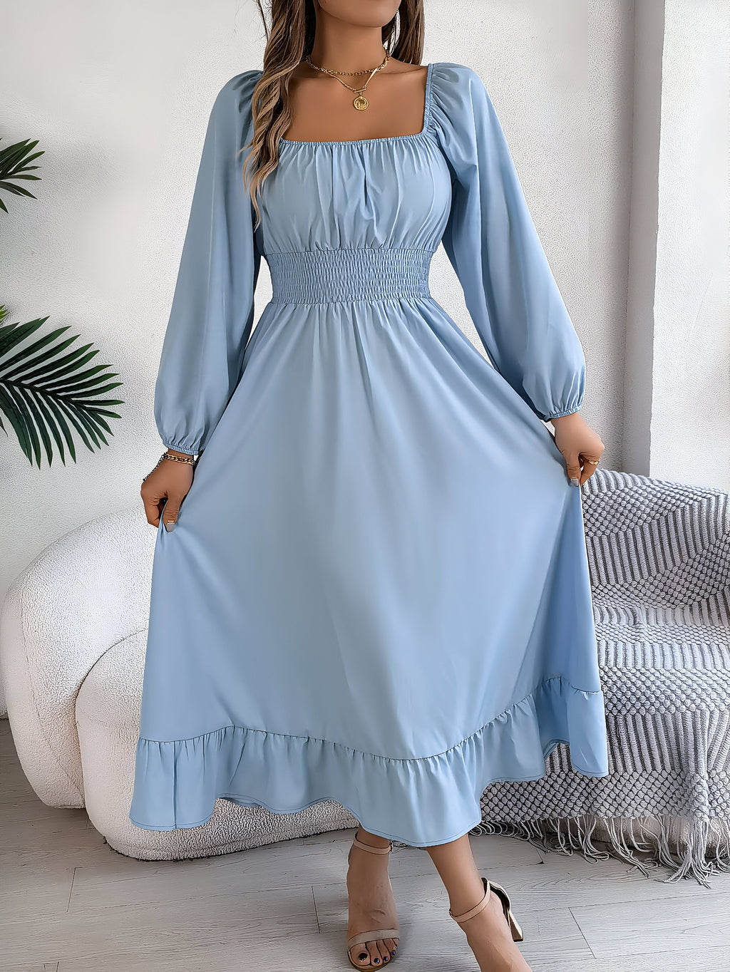 Robe longue bleue à manches longues, col carré, avec smocks à la taille, portée par une femme. Style élégant et décontracté, idéal pour l'été.