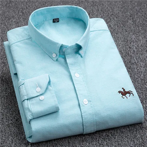 Chemise bleue en coton pour homme, pliée, avec logo brodé de cavalier, col boutonné, manches longues, posée sur fond gris.
