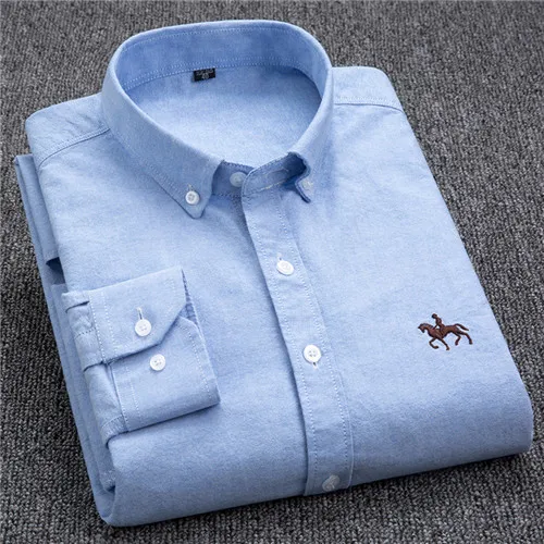 Chemise bleue en coton pour homme, manches longues, col boutonné, logo brodé, posée sur un fond gris. Mode élégante et décontractée.