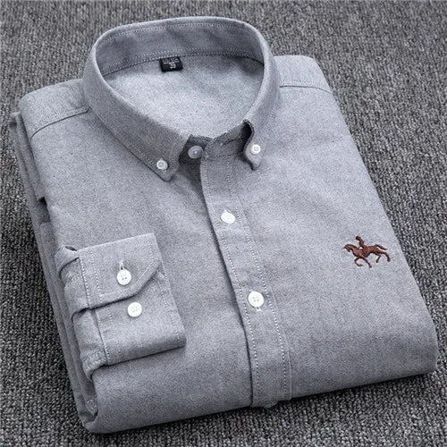 Chemise grise en coton pliée, avec col boutonné et logo brodé de cavalier, posée sur un fond en tissu gris. Mode homme élégante et classique.