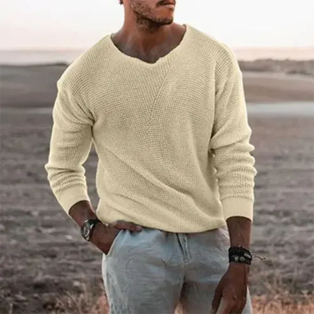 Homme portant un pull beige en maille, manches longues, sur fond de paysage désertique. Mode masculine, style décontracté, vêtements d'automne.