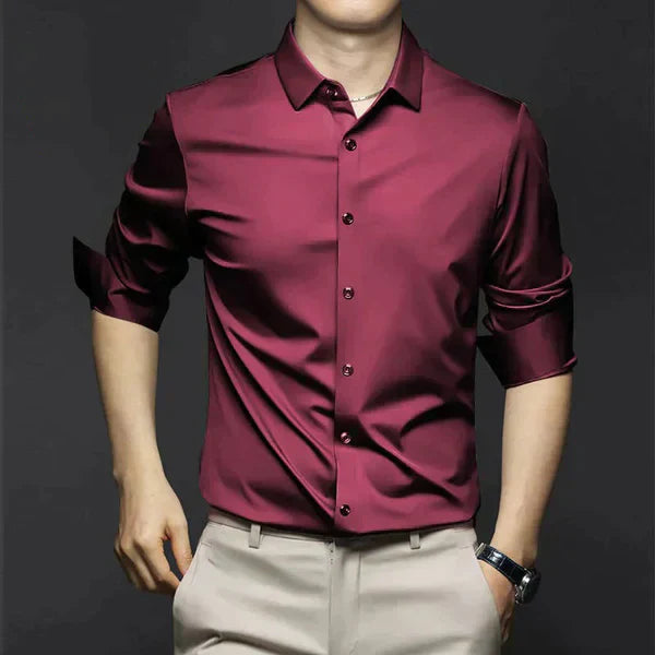 Homme portant une chemise en satin bordeaux élégante, manches retroussées, avec un pantalon beige, sur fond noir. Mode masculine chic et moderne.