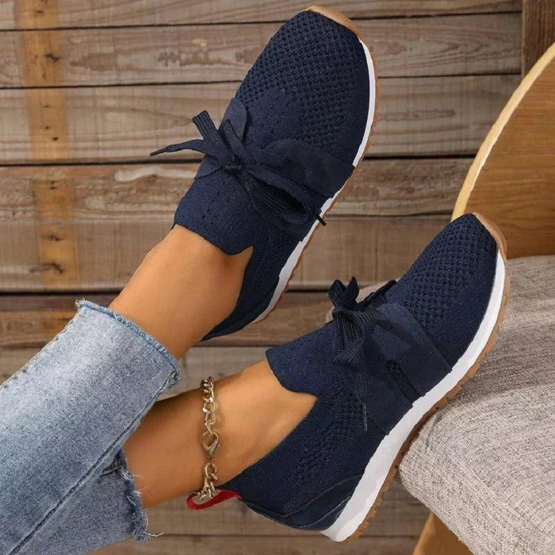 Chaussures de sport bleu marine pour femme avec lacets, semelle blanche, portées avec un jean. Style décontracté, tendance et confortable.