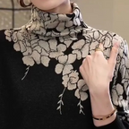 Femme portant un pull noir à col roulé avec motifs floraux beige, bague dorée et bracelet. Mode élégante, tendance automne-hiver.