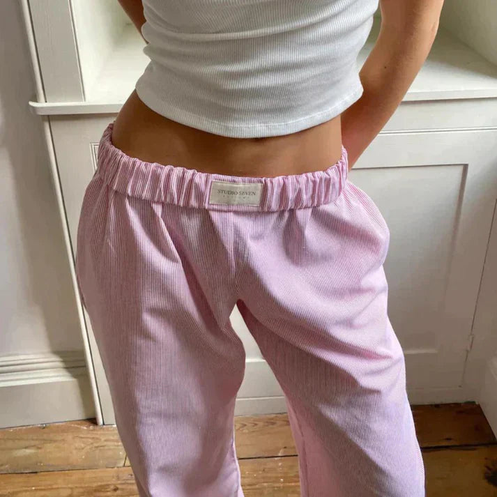 Jeune femme portant un pantalon rose en velours côtelé et un débardeur blanc, posant dans une pièce lumineuse. Mode décontractée, style tendance.