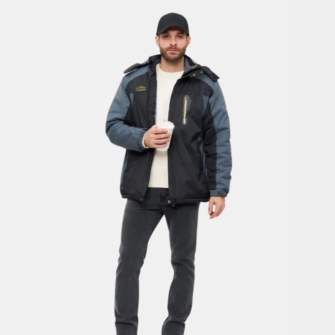 Homme portant une veste d'hiver noire et bleue, tenant un gobelet, casquette noire, sur fond blanc. Mode masculine, vêtements d'extérieur chauds.