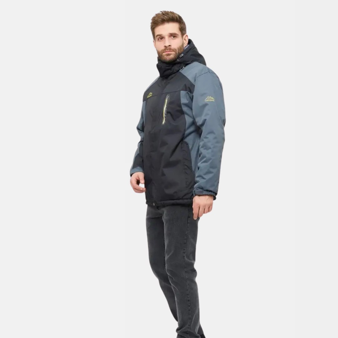 Homme portant une veste de ski imperméable bleu et noir, capuche incluse, idéale pour sports d'hiver. Mode hiver, vêtements de sport, tenue de ski.
