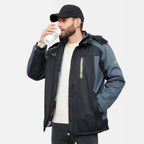 Homme portant une veste d'hiver noire et bleue, buvant un café à emporter, casquette noire, sur fond blanc. Mode masculine, vêtements d'extérieur.