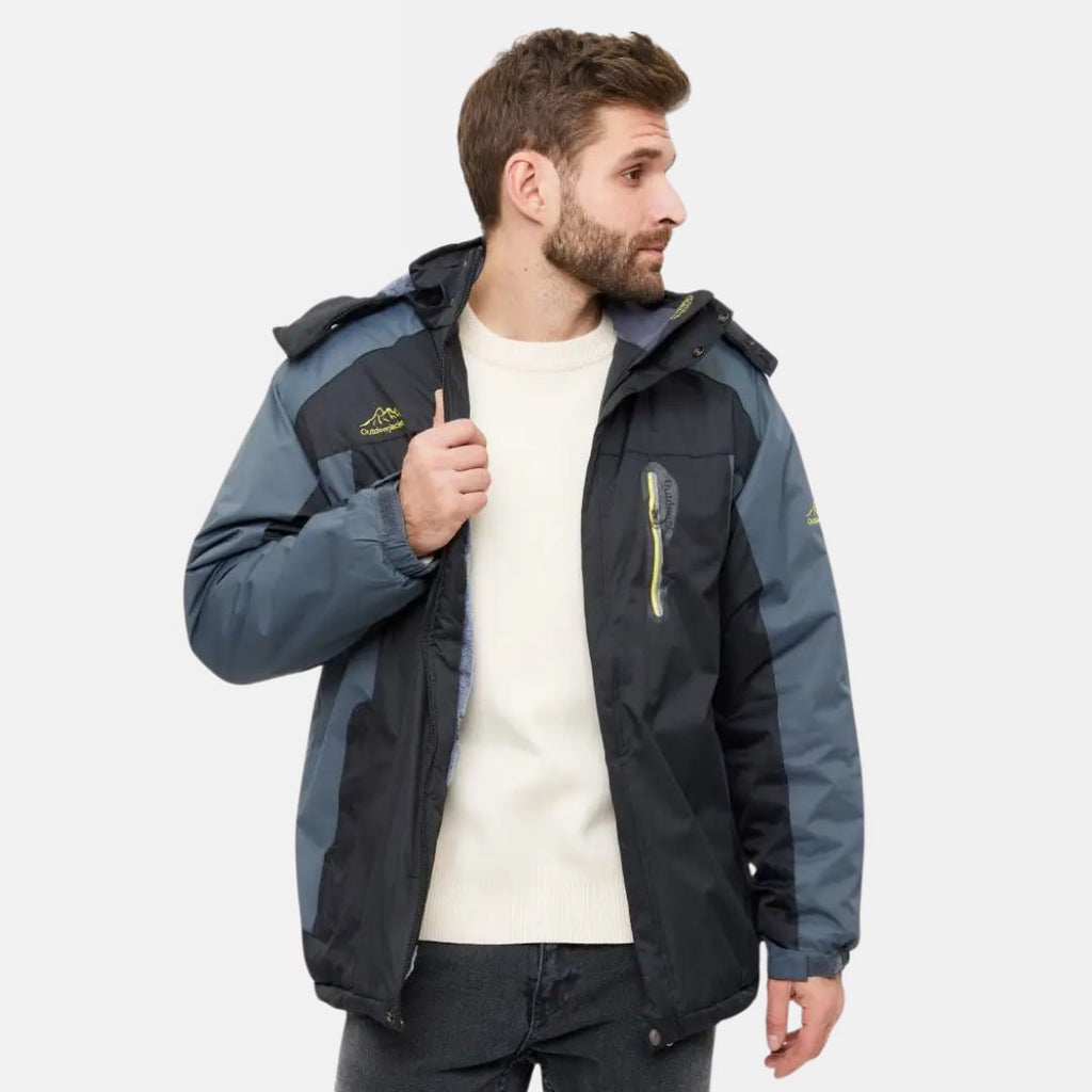 Homme portant une veste d'hiver imperméable bleu et noire, capuche amovible, fermeture éclair, idéale pour randonnée et activités extérieures.