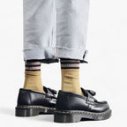 Chaussures noires en cuir avec semelles épaisses, portées avec des chaussettes rayées marron et jaunes et un jean clair retroussé. Mode urbaine tendance.
