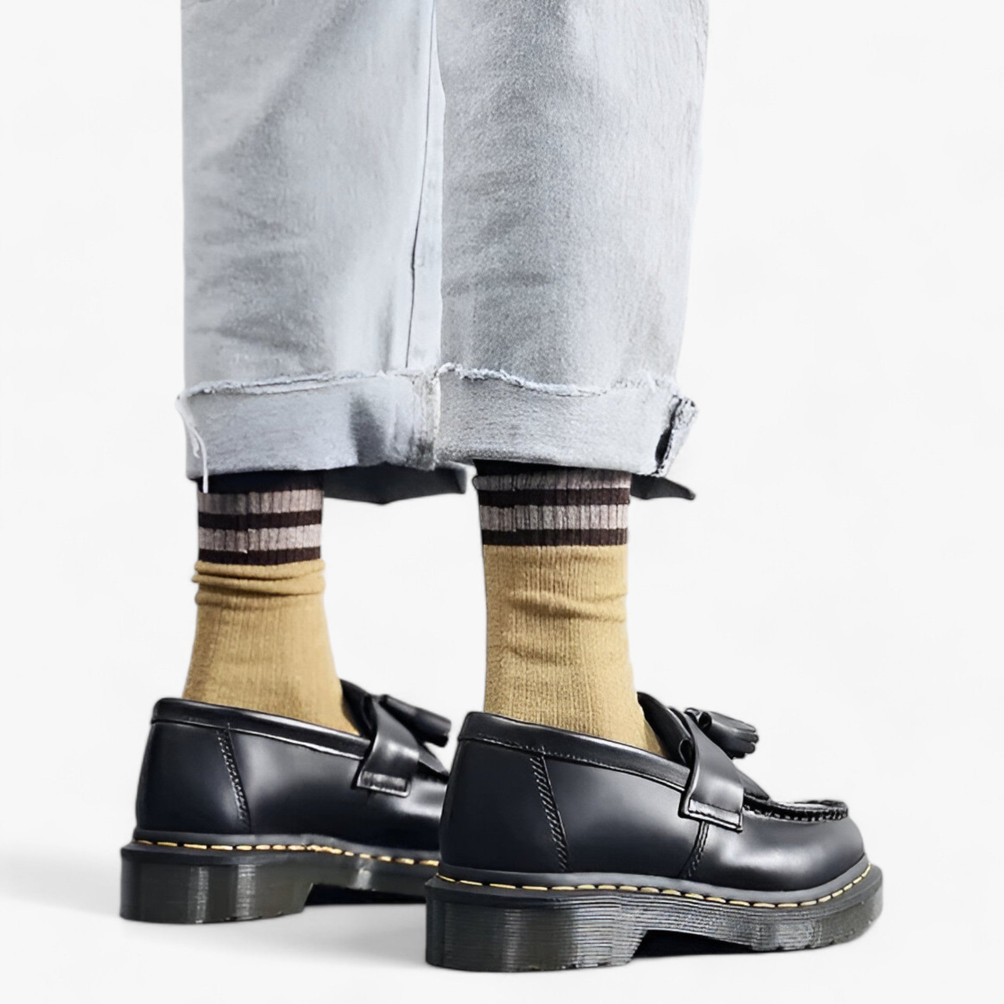 Chaussures noires en cuir avec semelles épaisses, portées avec des chaussettes rayées marron et jaunes et un jean clair retroussé. Mode urbaine tendance.