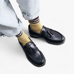 Chaussures mocassins en cuir noir avec pampilles, portées avec des chaussettes jaunes et un jean décontracté. Mode tendance, style urbain.