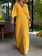 Robe longue jaune plissée élégante, manches larges, portée dans un intérieur moderne avec vue sur jardin. Mode féminine chic et tendance.