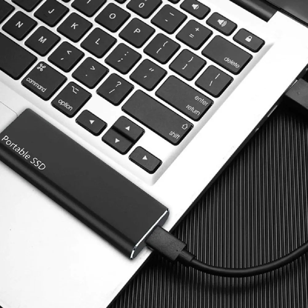 Disque SSD portable connecté à un ordinateur portable via un câble USB, sur un clavier argenté. Stockage externe rapide et compact.