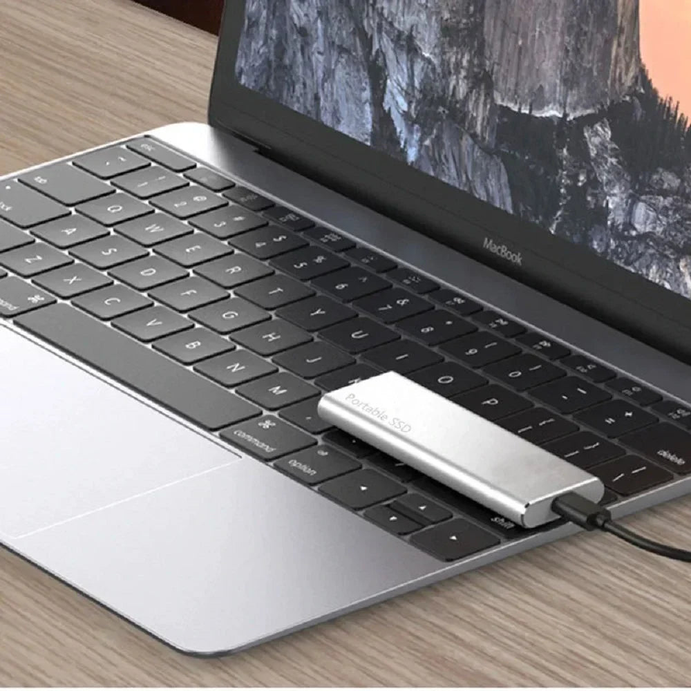 Ordinateur portable MacBook avec SSD externe connecté, posé sur un bureau en bois. Accessoire de stockage portable pour augmenter la capacité.