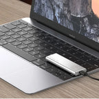 Ordinateur portable MacBook avec SSD externe connecté, posé sur un bureau en bois. Accessoire de stockage portable pour augmenter la capacité.