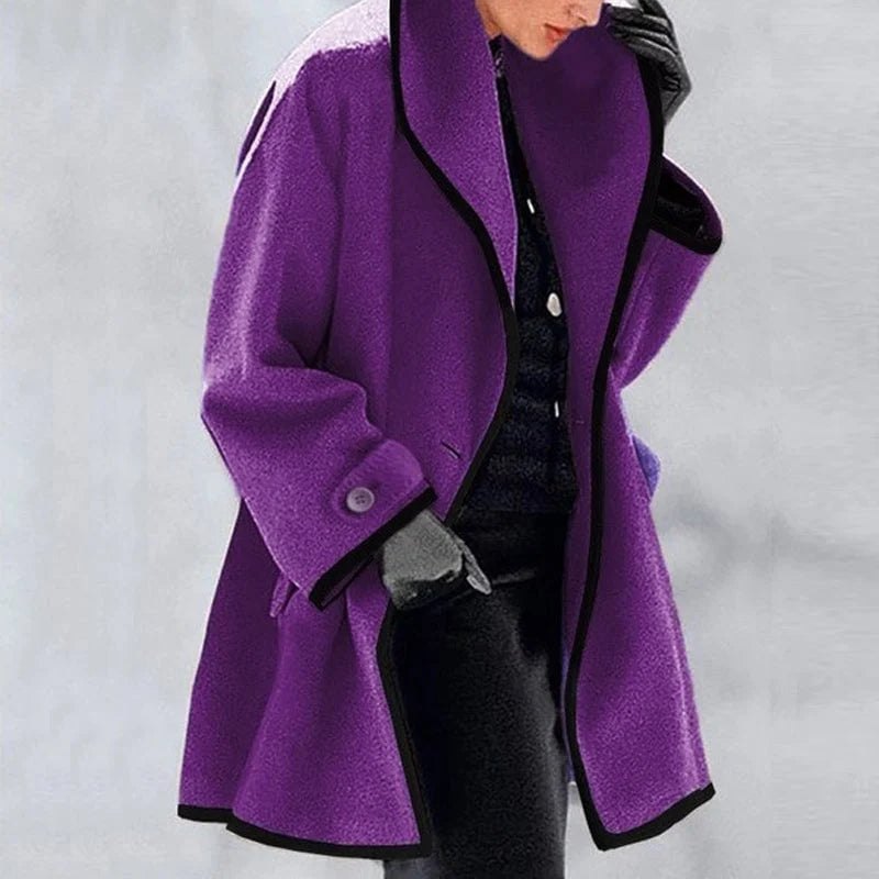 Manteau violet femme élégant, coupe ample, col large, bordure noire, porté avec gants gris et tenue noire, mode hiver chic.