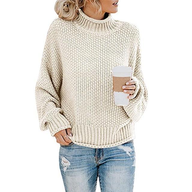 Femme en pull en maille beige, tenant un gobelet de café, portant un jean déchiré. Mode automne-hiver, style décontracté et tendance.