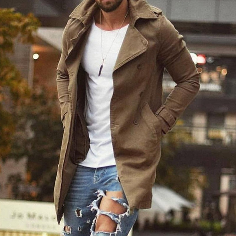 Homme portant un trench-coat marron, t-shirt blanc et jeans déchirés, style urbain moderne, mode masculine automne, extérieur urbain.