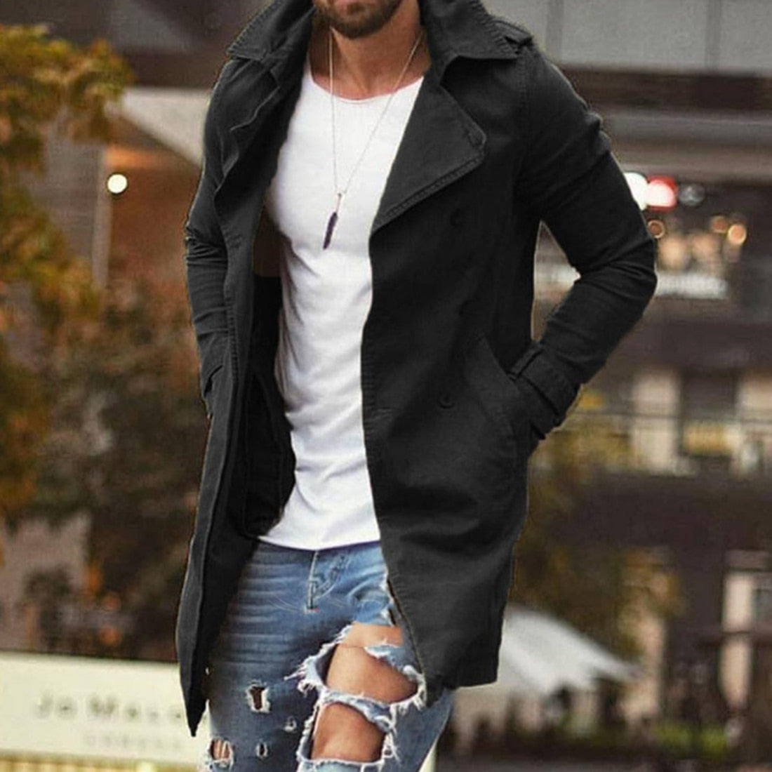 Homme en manteau noir élégant, t-shirt blanc, jeans déchiré, marchant en ville. Mode masculine, style urbain, tendance automne-hiver.