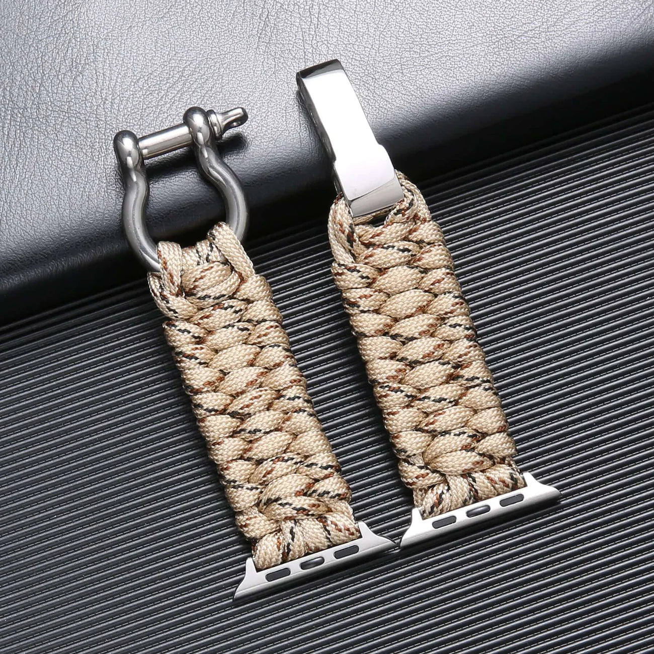 Bracelet de montre en paracorde beige tressée avec fermoir en acier inoxydable, posé sur une surface texturée noire. Accessoire mode robuste.