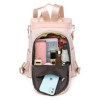 Sac à dos beige ouvert avec compartiments organisés, contenant un smartphone, portefeuille rose, livres, bouteille d'eau, et cosmétiques. Accessoire mode pratique.