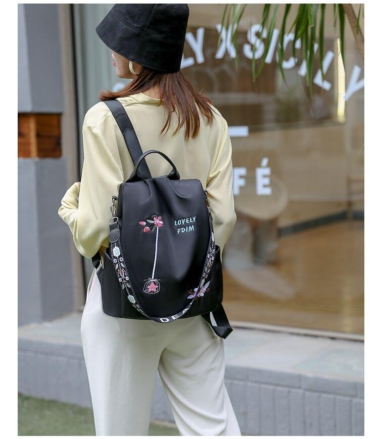 Femme portant un sac à dos noir avec motifs floraux, devant un café. Mode urbaine, style décontracté, accessoires tendance.