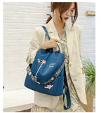 Femme portant un sac à dos bleu avec motifs floraux, tenue élégante avec blazer beige et robe à motifs. Mode féminine, accessoires tendance.