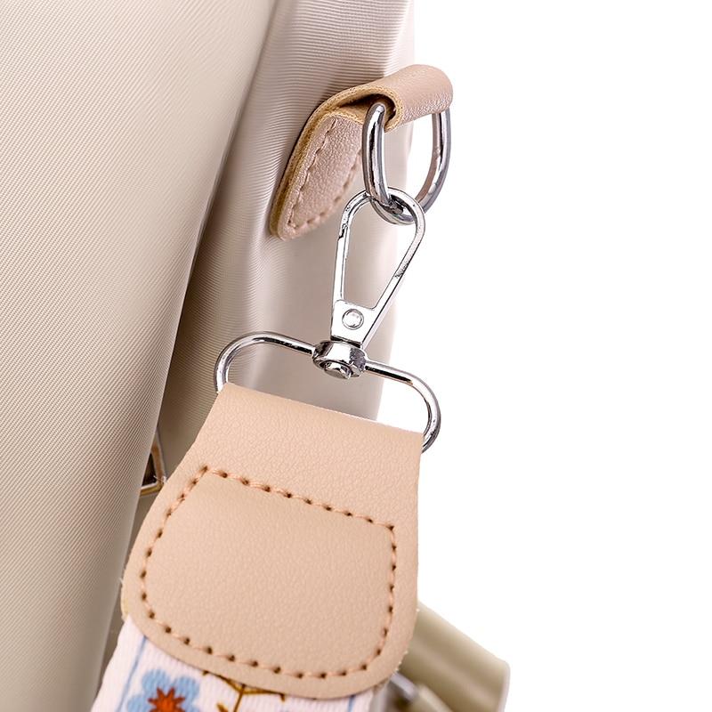 Gros plan sur un sac à main beige avec une sangle amovible à motif floral, crochet en métal argenté. Accessoire de mode élégant et pratique.