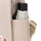 Sac à dos beige avec poche latérale contenant un parapluie rayé bleu et blanc et une bouteille noire. Accessoire pratique et élégant.