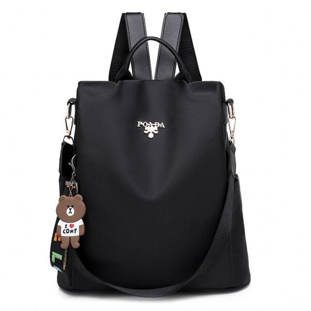 Sac à dos noir élégant avec breloque ours en peluche, bretelles ajustables et logo argenté. Accessoire mode tendance pour femmes.