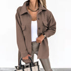Femme portant une veste marron élégante, chemise blanche, pantalon en cuir beige, tenant un sac à carreaux. Mode automne chic et tendance.
