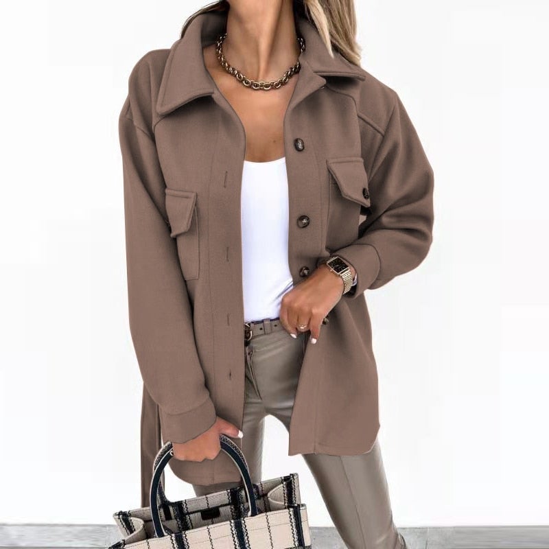 Femme portant une veste marron élégante, chemise blanche, pantalon en cuir beige, tenant un sac à carreaux. Mode automne chic et tendance.
