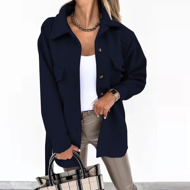 Femme portant une veste bleu marine élégante, chemise blanche, pantalon beige, collier doré, tenant un sac à carreaux. Mode chic et moderne.
