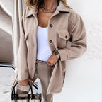 Femme portant une surchemise beige élégante, chemise blanche, pantalon assorti, sac à main à carreaux, montre dorée, collier chaîne. Mode automne chic.