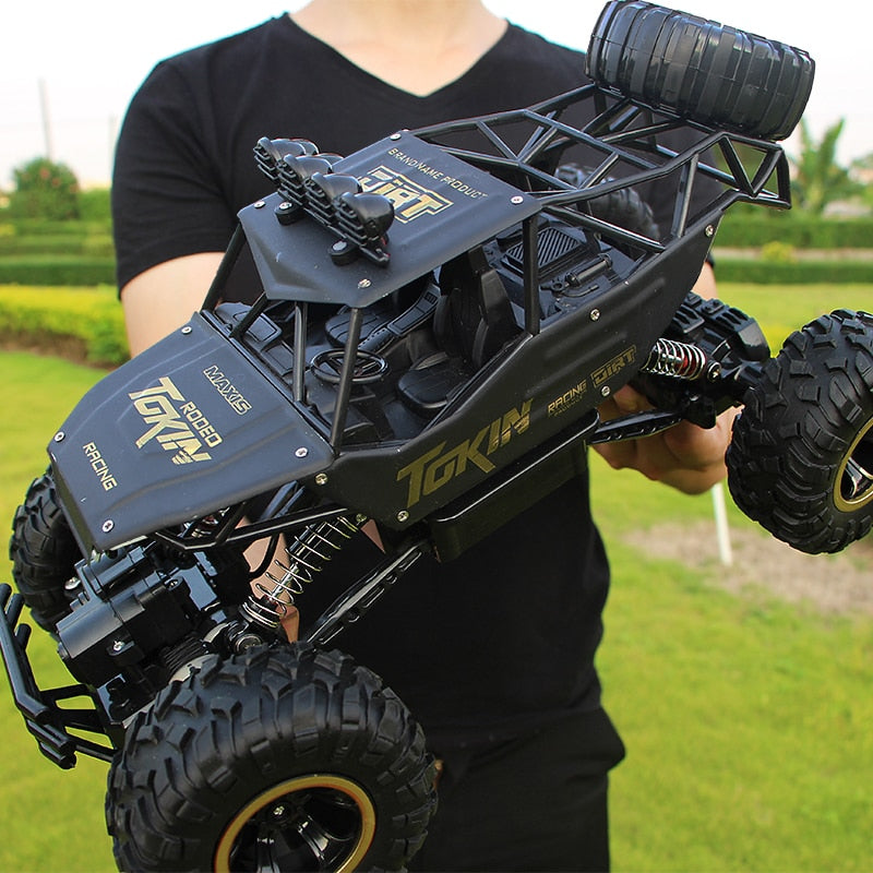 Voiture télécommandée tout-terrain noire, design robuste, pneus larges, tenue par une personne en extérieur. Modèle de course RC performant.